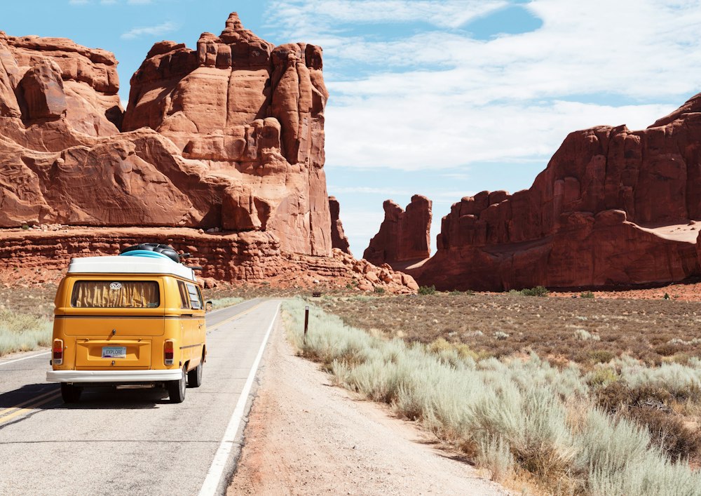 Yellow camper van on a desert road among red rocks